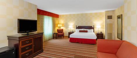 A hotel room with a bed, a TV, a desk, a chair, a sofa, and a mirror.