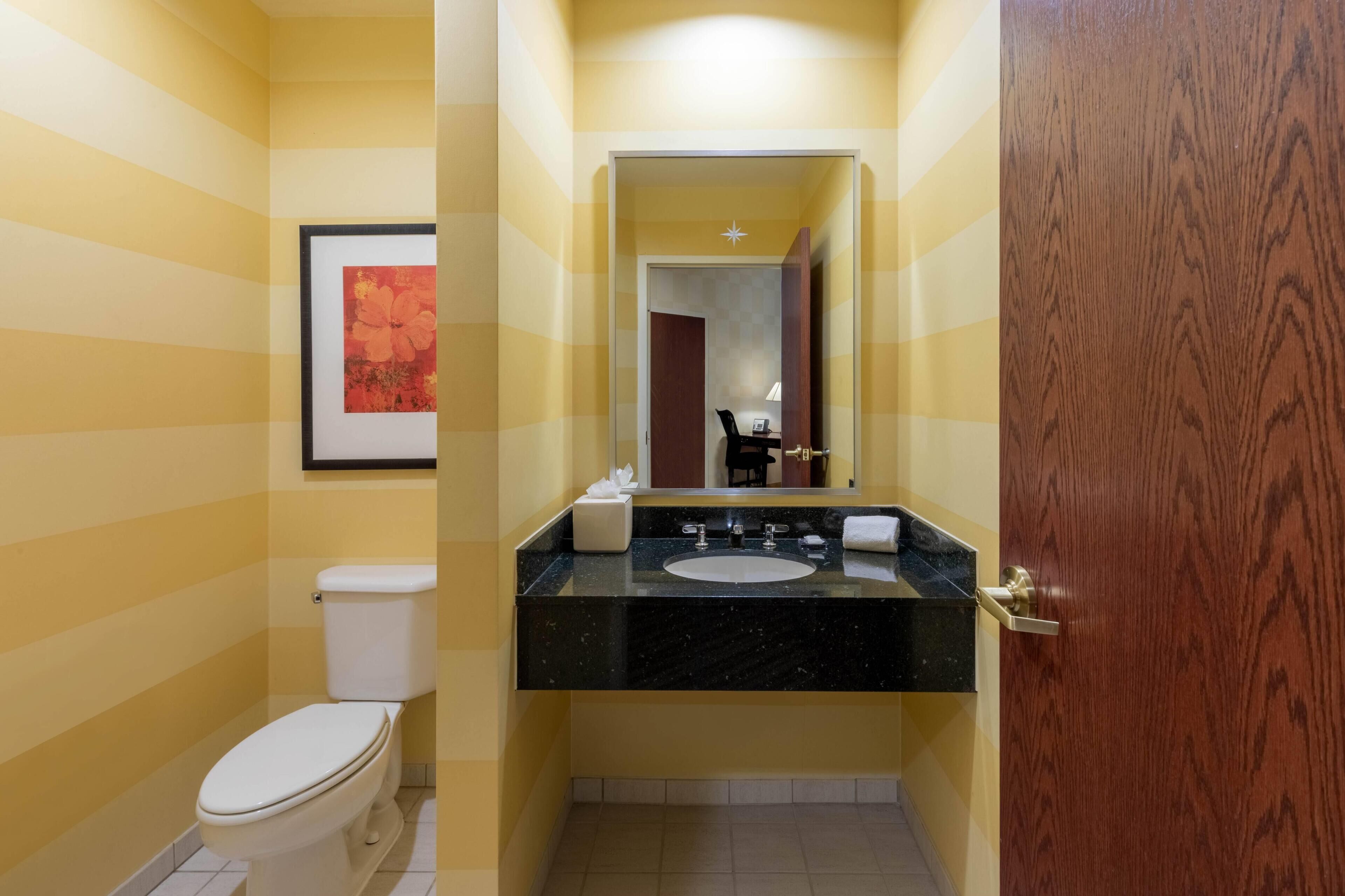A bathroom with a striped wall, a toilet, a sink with a mirror, and a wooden door.