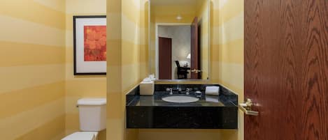 A bathroom with a striped wall, a toilet, a sink with a mirror, and a wooden door.