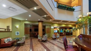 A hotel lobby with a high ceiling, multiple seating areas, and a staircase leading to an upper level. - Wyndham Grand Oklahoma City Downtown (Oklahoma City)