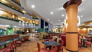 Un vestíbulo de hotel con varias zonas de comedor, una escalera central y un pilar grande.