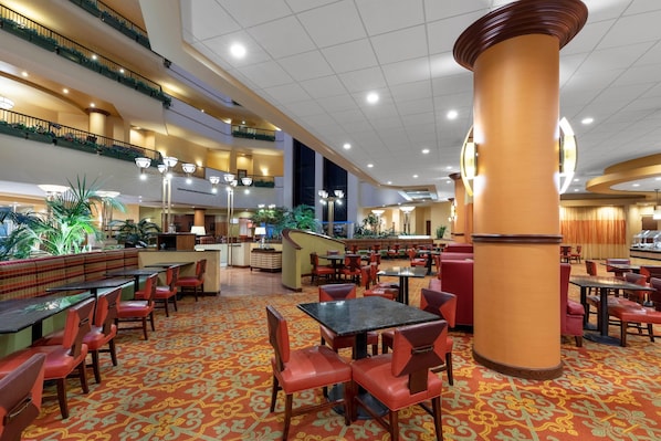 A hotel lobby with multiple dining areas, a central staircase, and a large pillar. - Wyndham Grand Oklahoma City Downtown (Oklahoma City)
