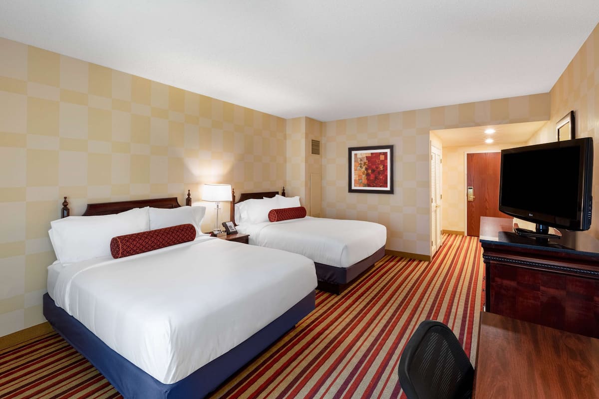 A hotel room with two beds, a desk with a TV, and a door leading to a bathroom.