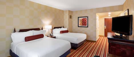 A hotel room with two beds, a desk with a TV, and a door leading to a bathroom.