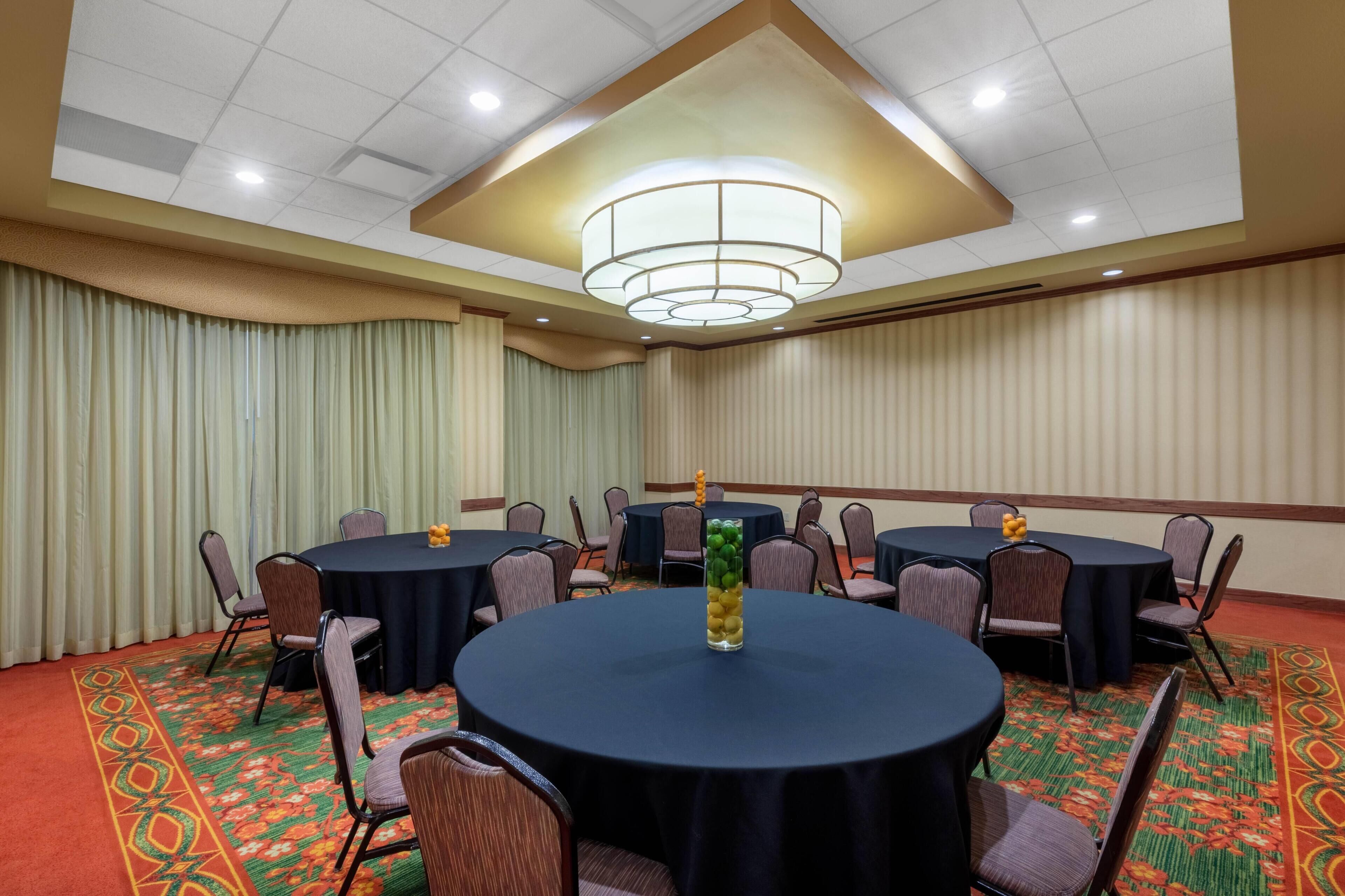 Un salón de conferencias con mesas redondas, sillas y un jarrón decorativo.