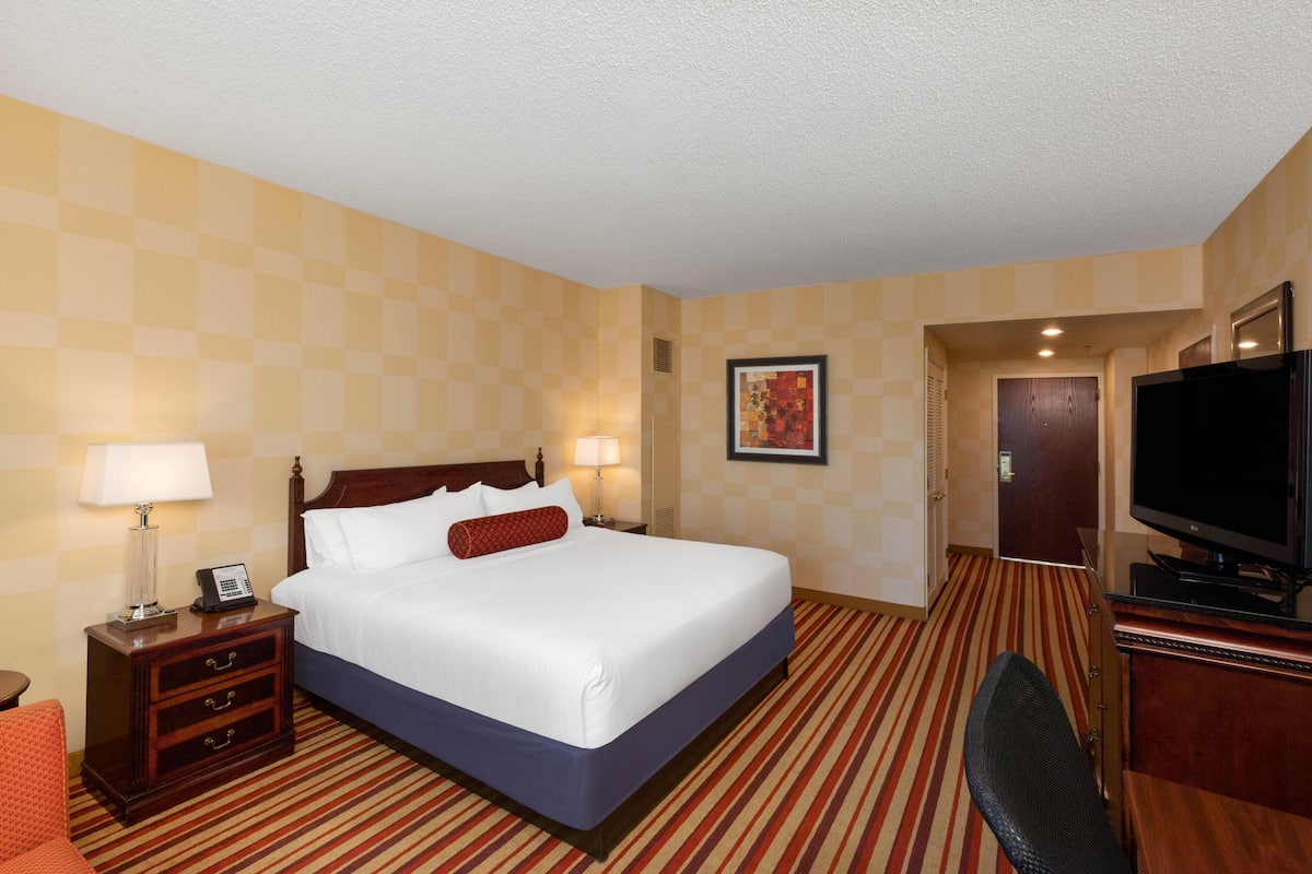 A hotel room with a bed, bedside tables, a television, and a door leading to another room.