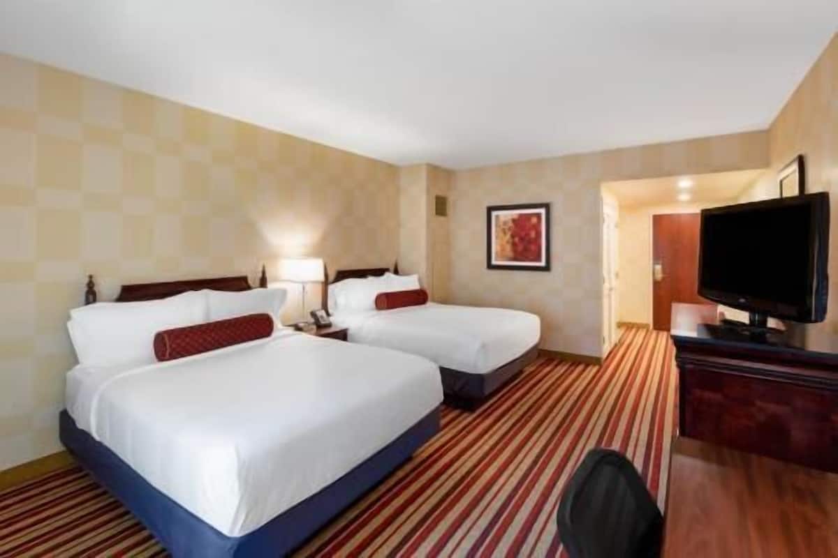 A hotel room with two beds, a television, a desk, and a carpeted floor.