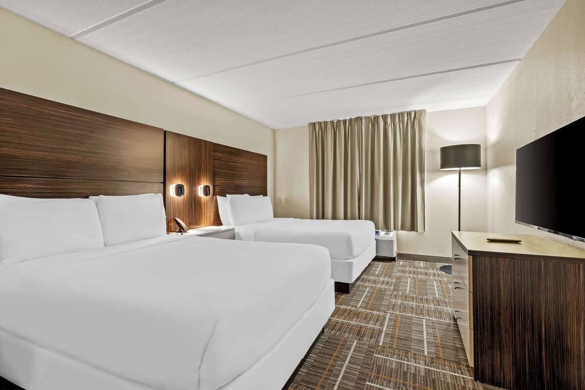 Une chambre d’hôtel avec deux lits, un téléviseur à écran plat, un bureau et une lampe.