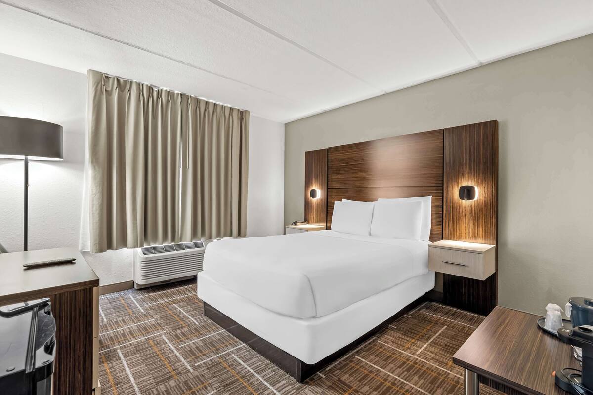 Une chambre d’hôtel avec un grand lit, des tables de chevet, un bureau, une lampe, un radiateur et des rideaux.