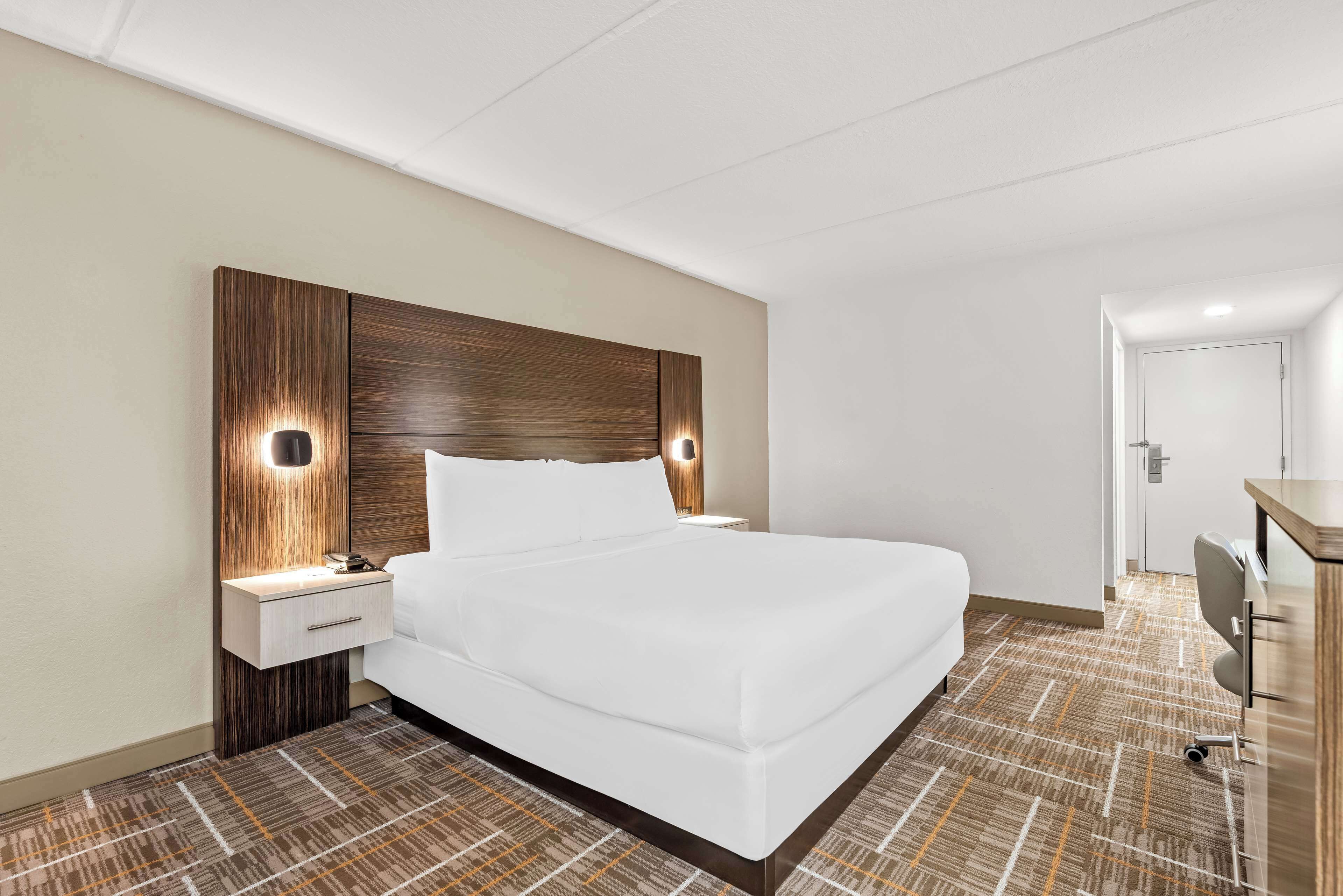 A hotel room with a large bed, a wooden headboard, bedside tables with lamps, and a carpeted floor.