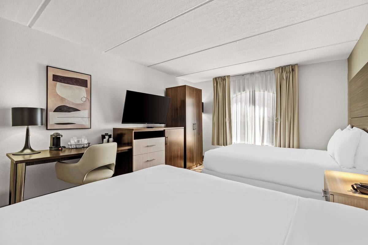 Une chambre d’hôtel avec un lit, un bureau avec un ordinateur, une chaise, une télévision et une fenêtre avec des rideaux.