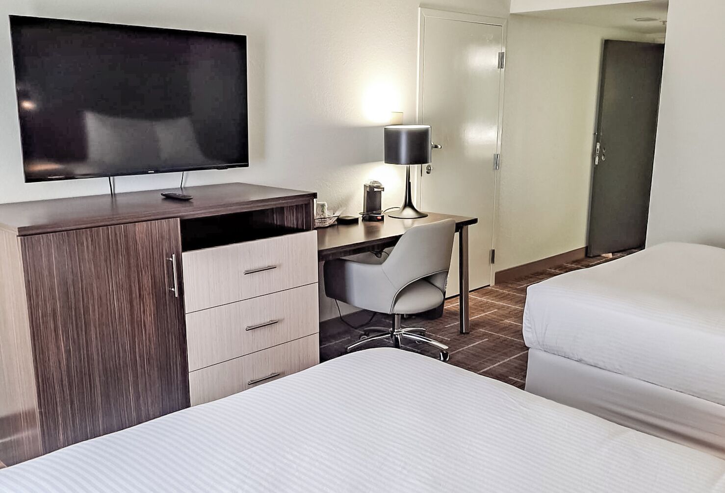 A hotel room with a bed, a desk with a chair, a television, and a wardrobe.
