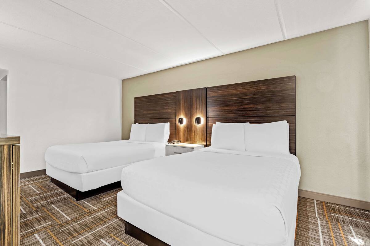 Une chambre d’hôtel avec deux lits, une table de chevet et un luminaire fixé au mur.
