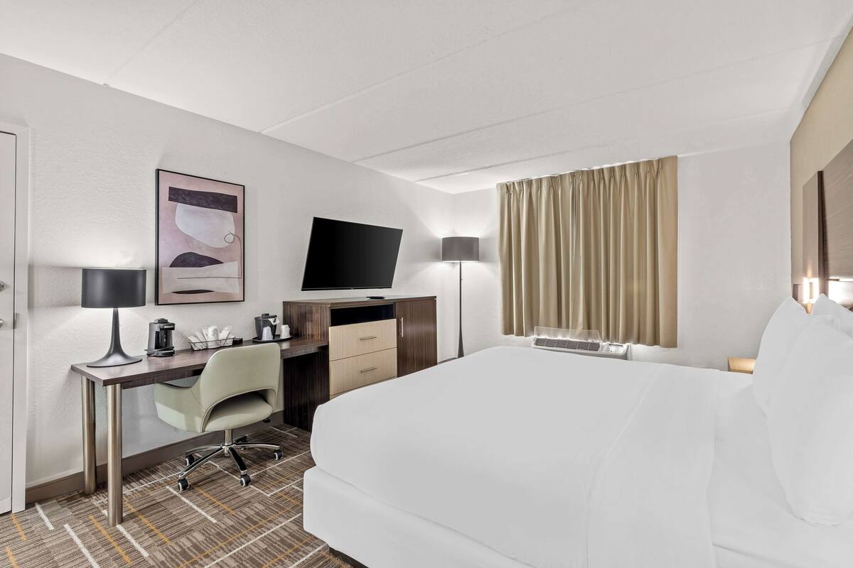 Une chambre d’hôtel équipée d’un lit, d’un bureau, d’une chaise, d’une télévision, d’une lampe et de rideaux.