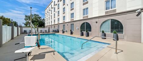 A hotel with a swimming pool, outdoor seating, and a large building with multiple windows.