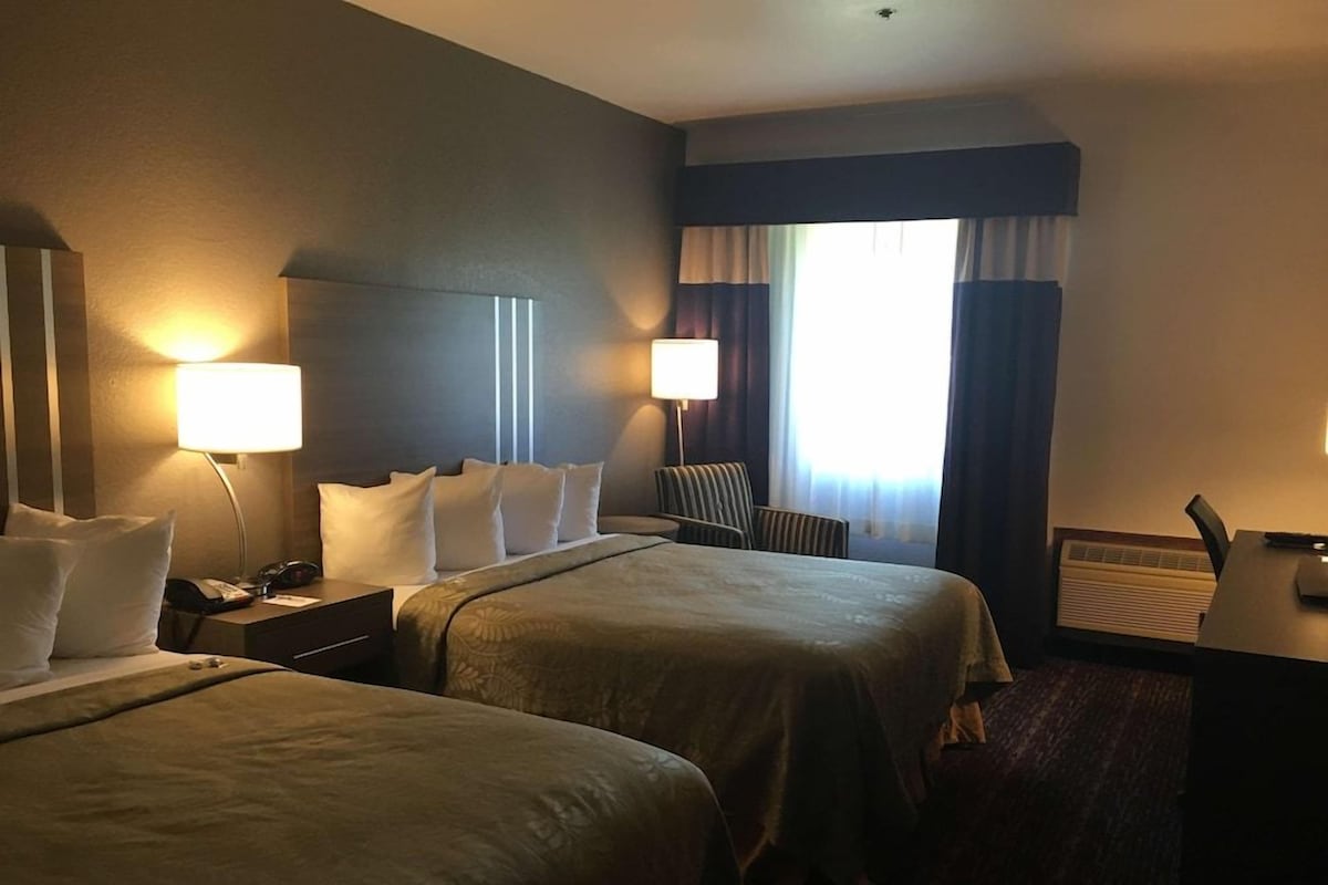 Habitación de hotel con dos camas, lámparas de noche, un escritorio con silla y una ventana con cortinas.
