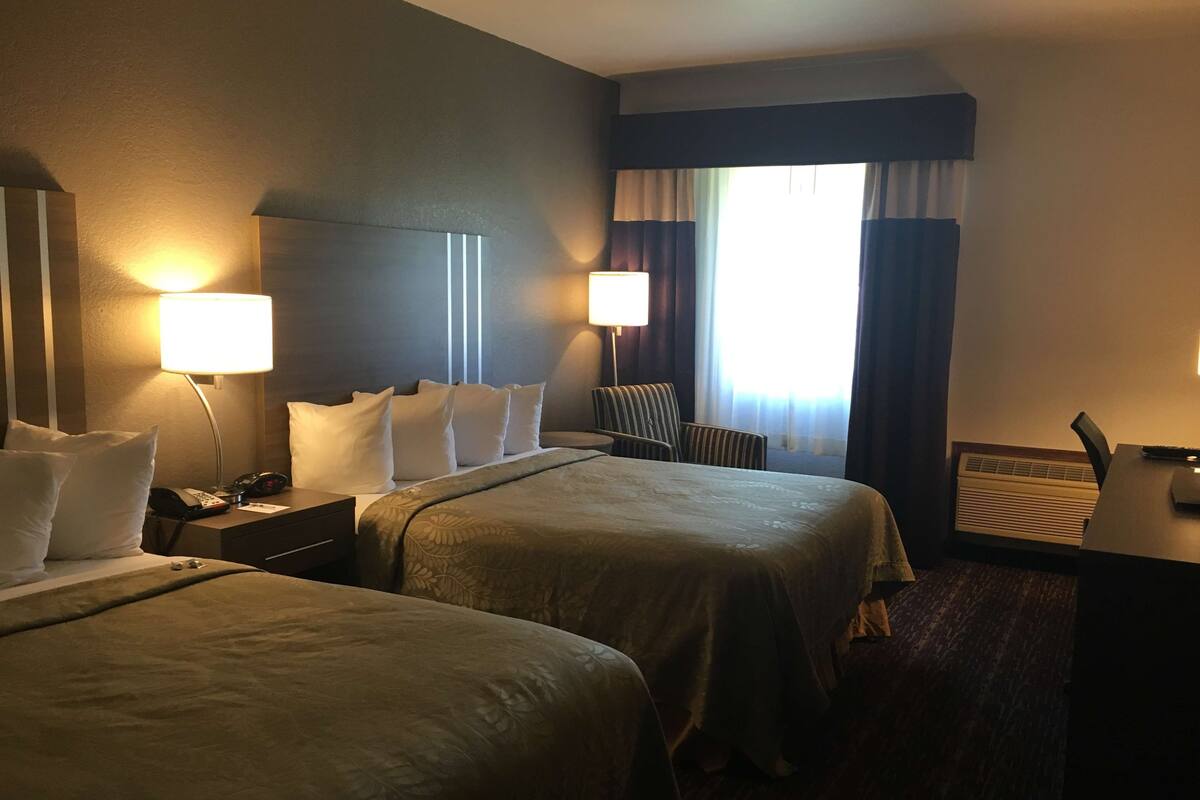 Habitación de hotel con dos camas, un escritorio, una silla y una ventana con cortinas.