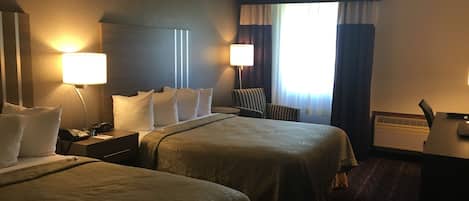 Habitación de hotel con dos camas, un escritorio, una silla y una ventana con cortinas.