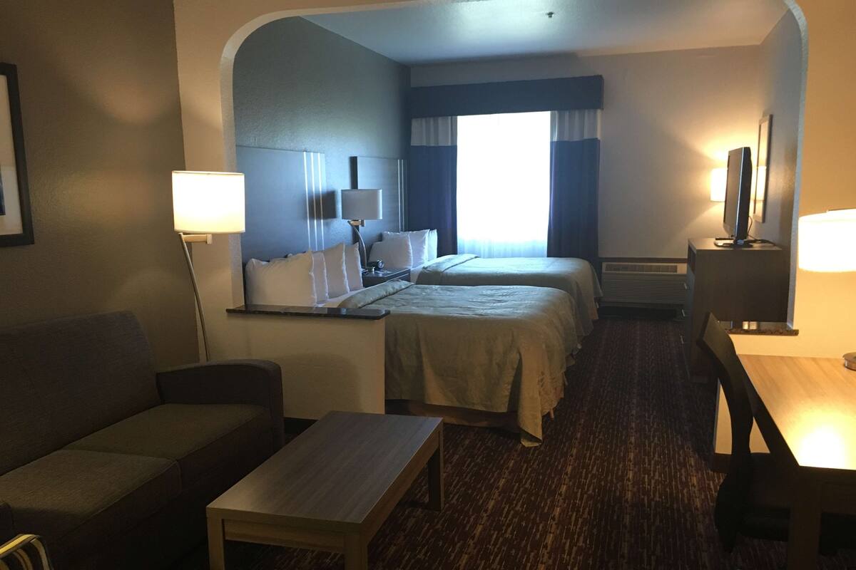 Habitación de hotel con dos camas, un escritorio, una silla, un sofá y un televisor.