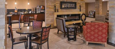 A hotel lobby with a dining area, a fireplace, and a kitchen in the background.