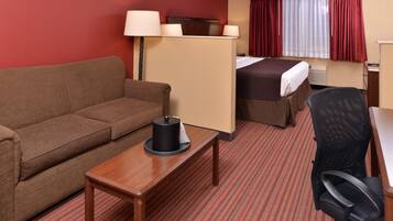 A hotel room with a sofa, a small table with a lamp, a bed, a desk, and a chair.