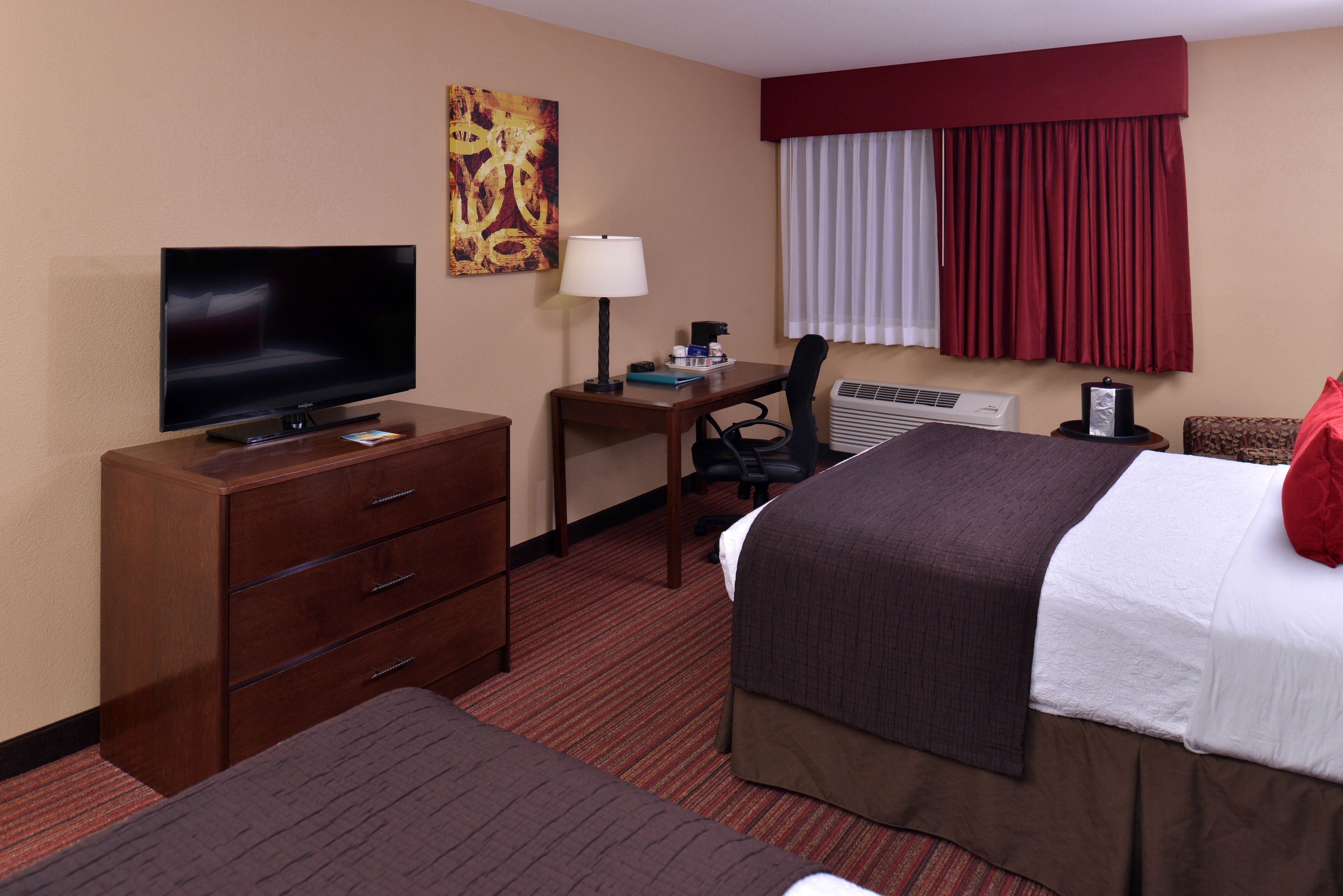 A hotel room with a bed, a desk with a lamp, a television, and a dresser.