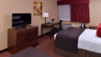 A hotel room with a bed, a desk with a lamp, a television, and a dresser.