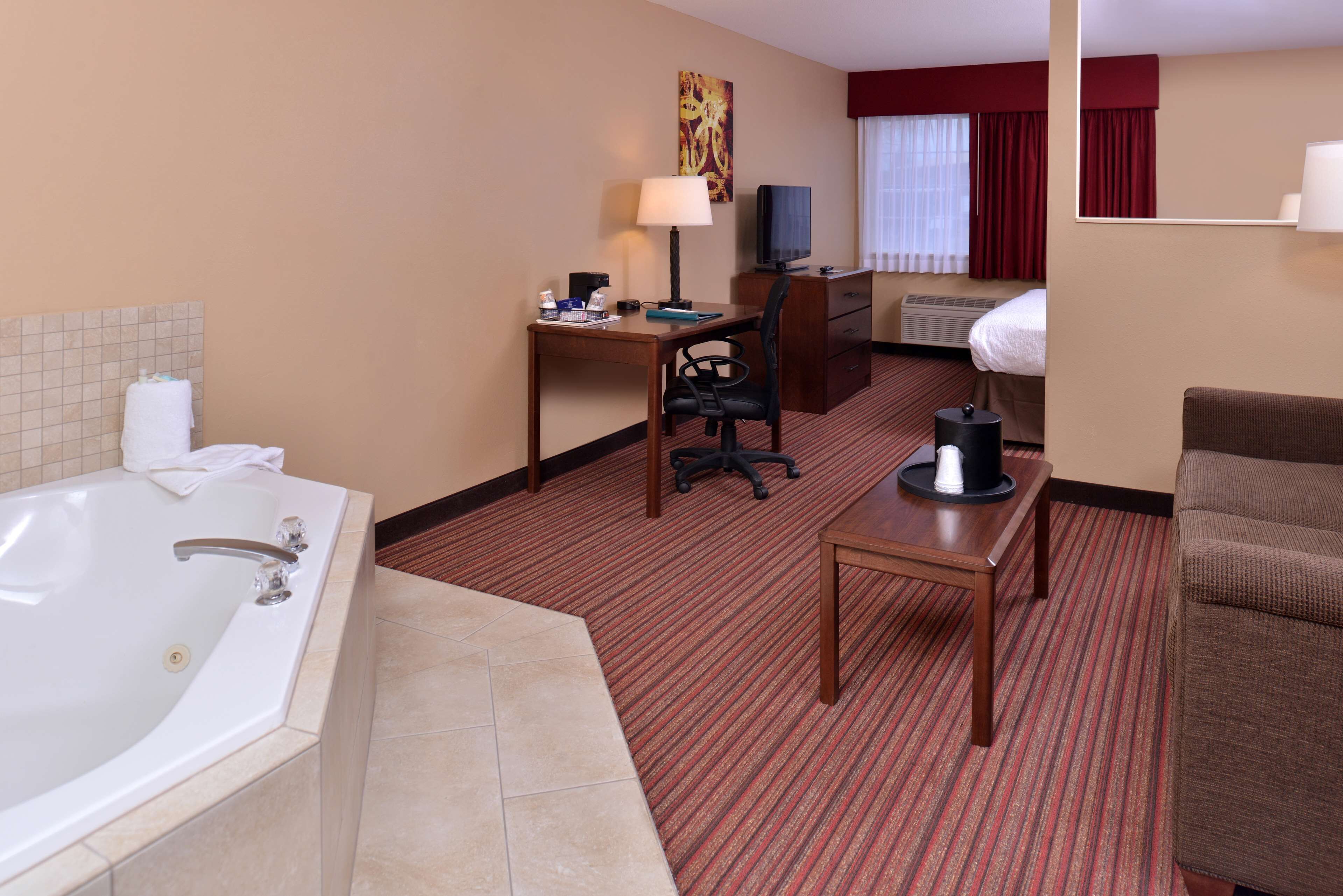Habitación de hotel con una bañera grande, un escritorio con ordenador, una silla, una mesita con cafetera y un sofá.