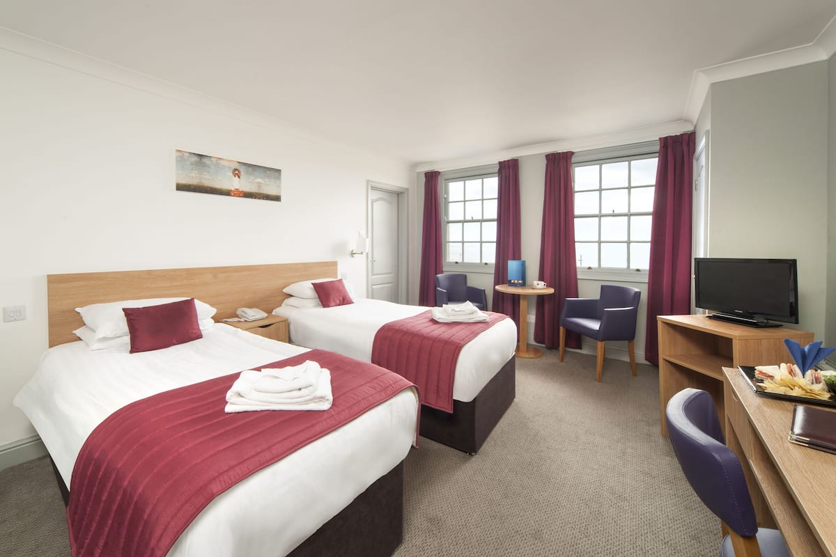 Quarto de hotel com duas camas, uma escrivaninha, uma televisão e uma janela com cortinas.
