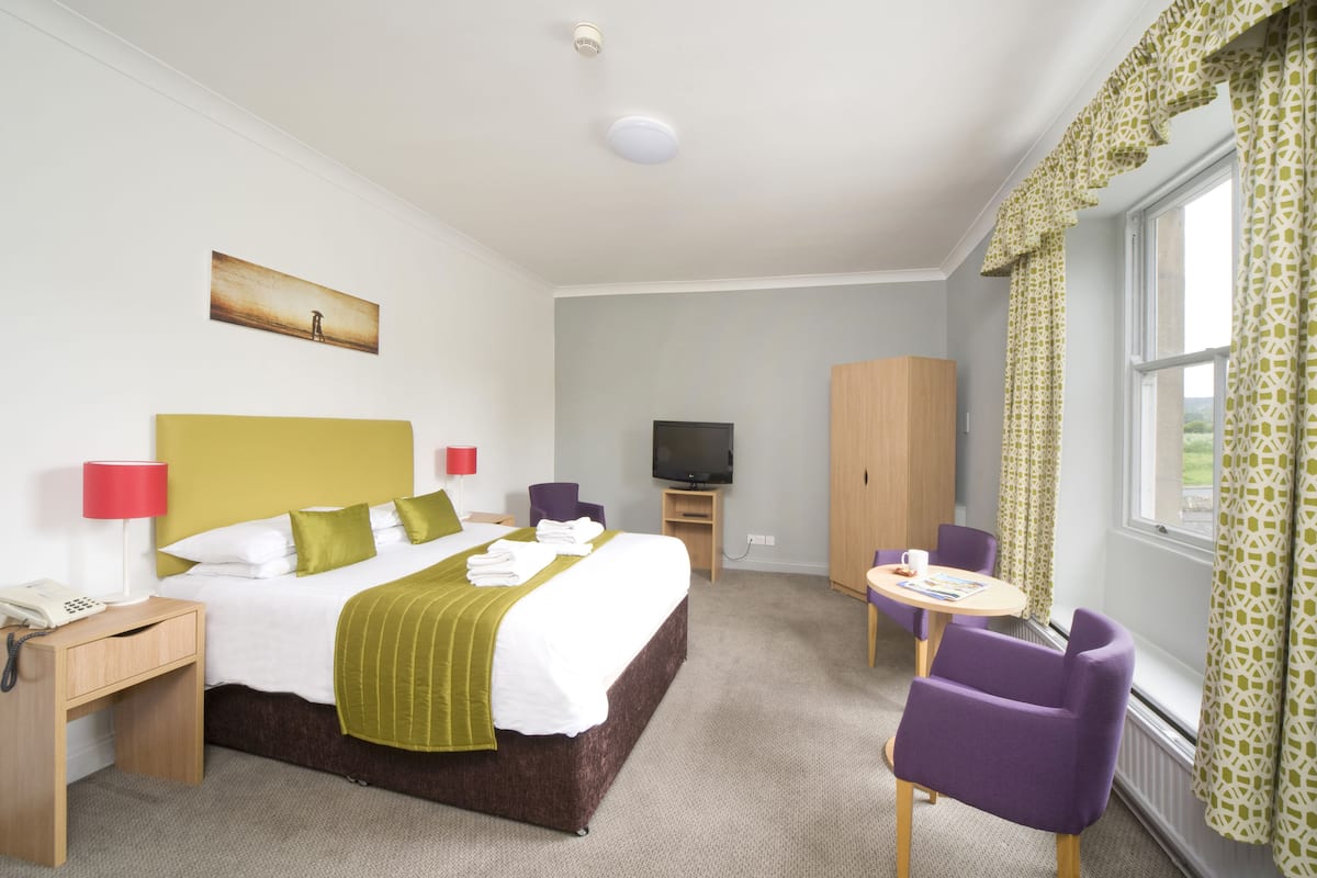 Quarto de hotel com cama, televisão, guarda-roupa, escrivaninha e cadeira.