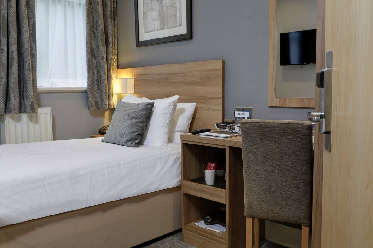 Ein Hotelzimmer mit Bett, Nachttisch, Lampe, Fernseher und Spiegel.