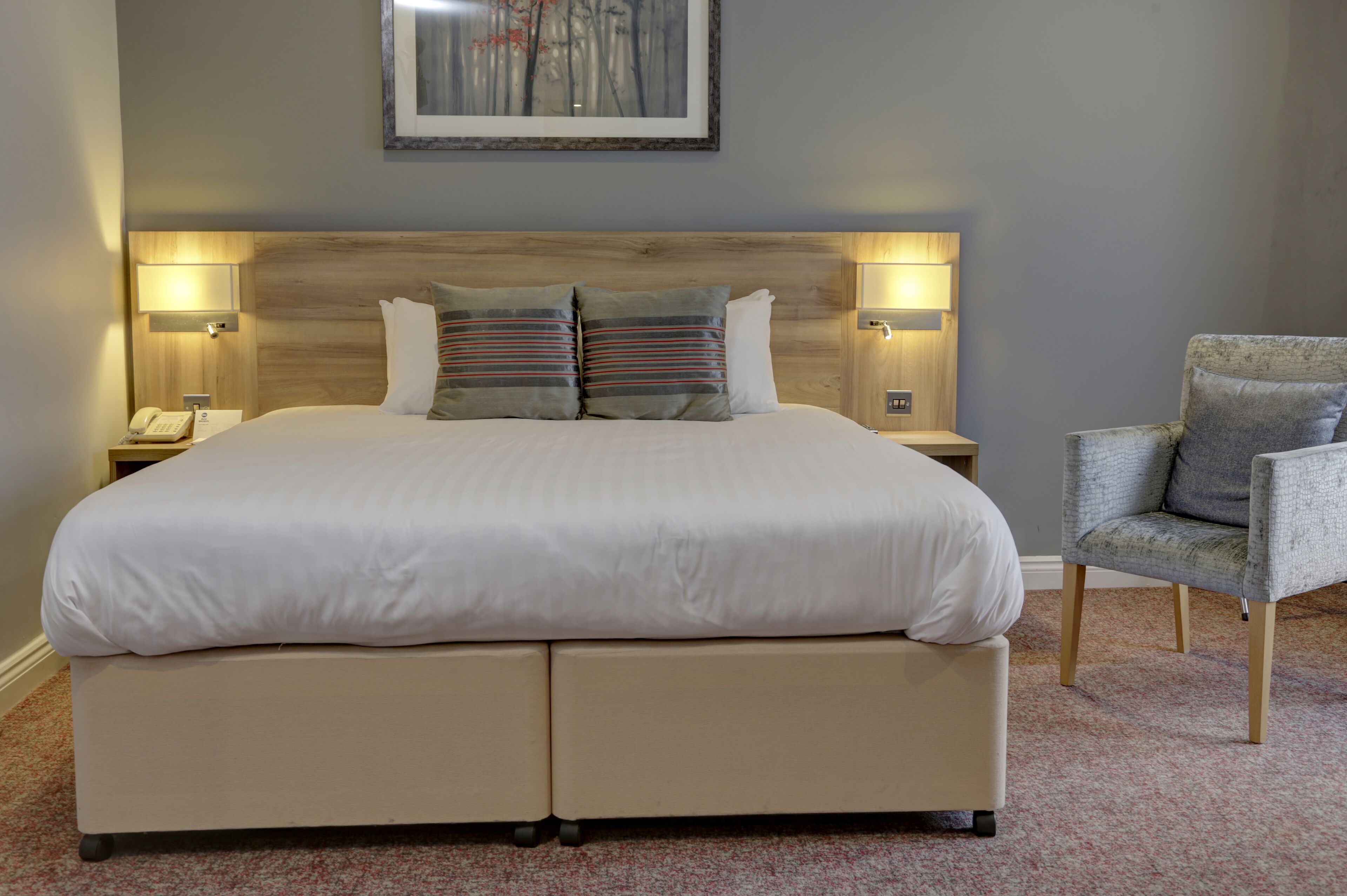 A large bed with a wooden headboard, two bedside lamps, and a chair.