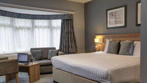 Une chambre d’hôtel avec un grand lit, un canapé, un bureau avec un ordinateur portable et une fenêtre avec des rideaux.