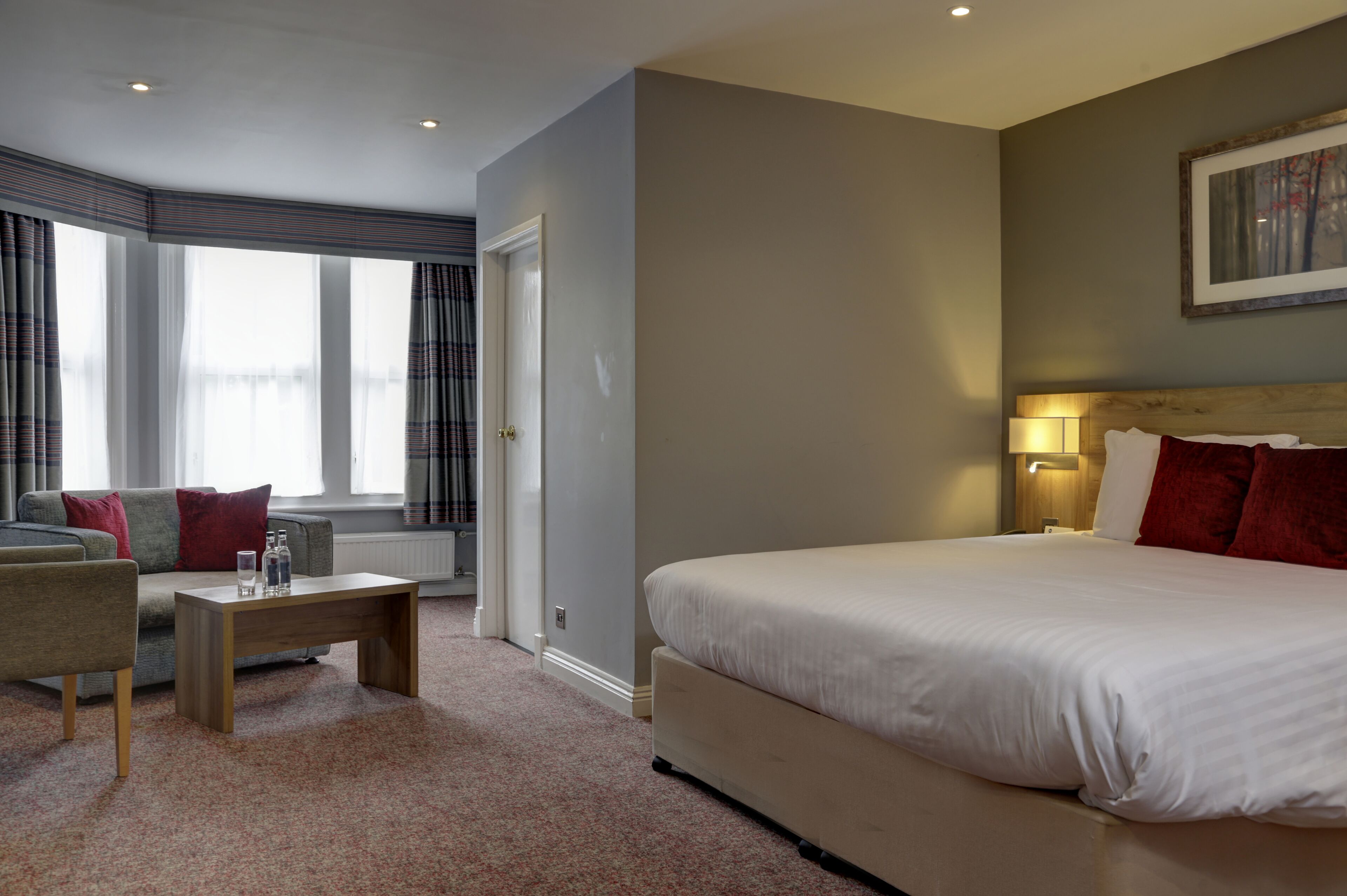 Habitación de hotel con una cama grande, un sofá, una mesita y una ventana con cortinas.