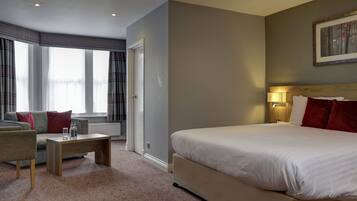 Een hotelkamer met een groot bed, een sofa, een kleine tafel en een raam met gordijnen.