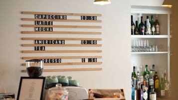 A bar area with a drink menu on the wall listing prices for cappuccino, latte, mocha, americano, tea, and espresso.