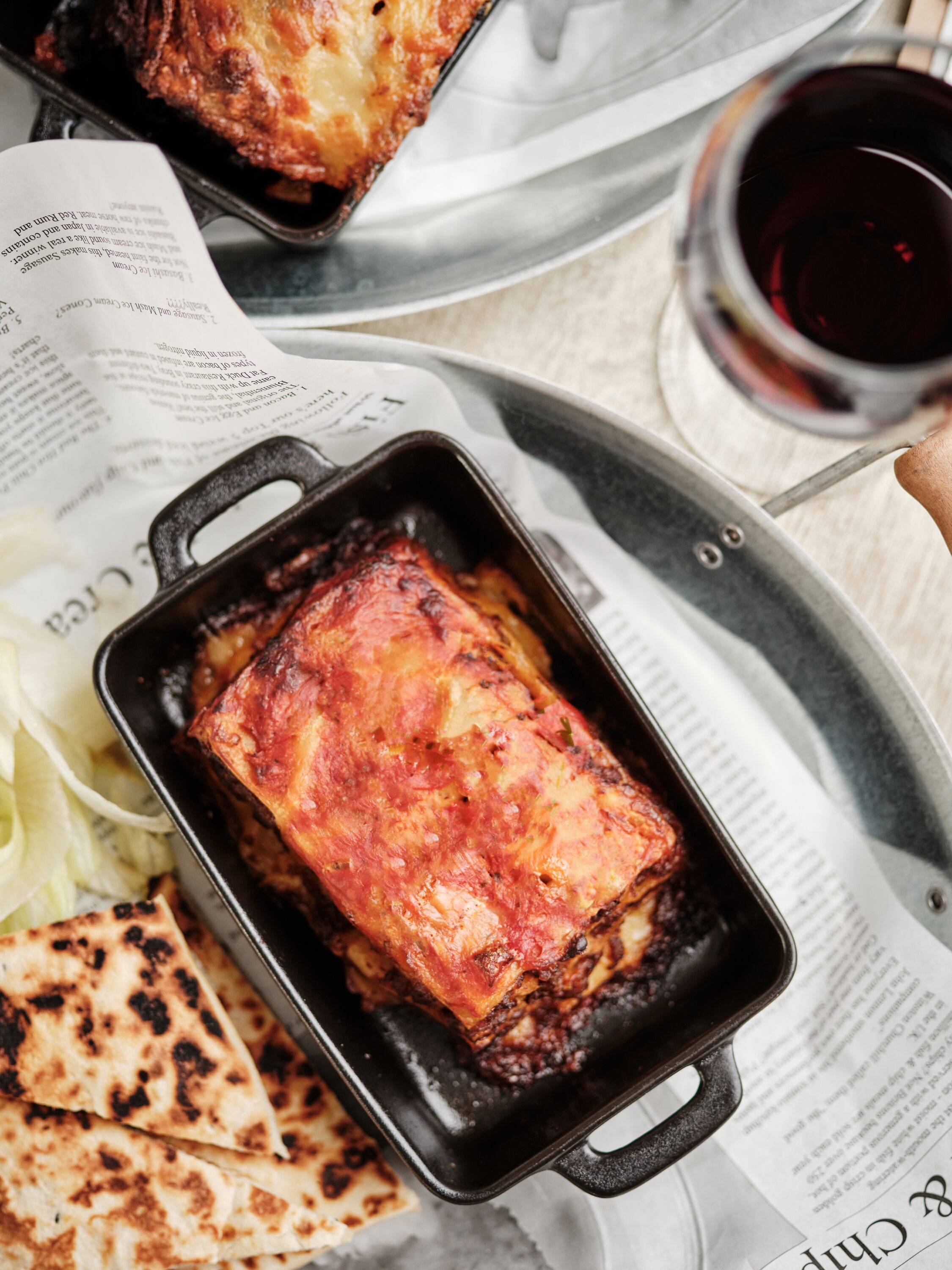 A dish in a cast iron skillet on a tray with a newspaper underneath.