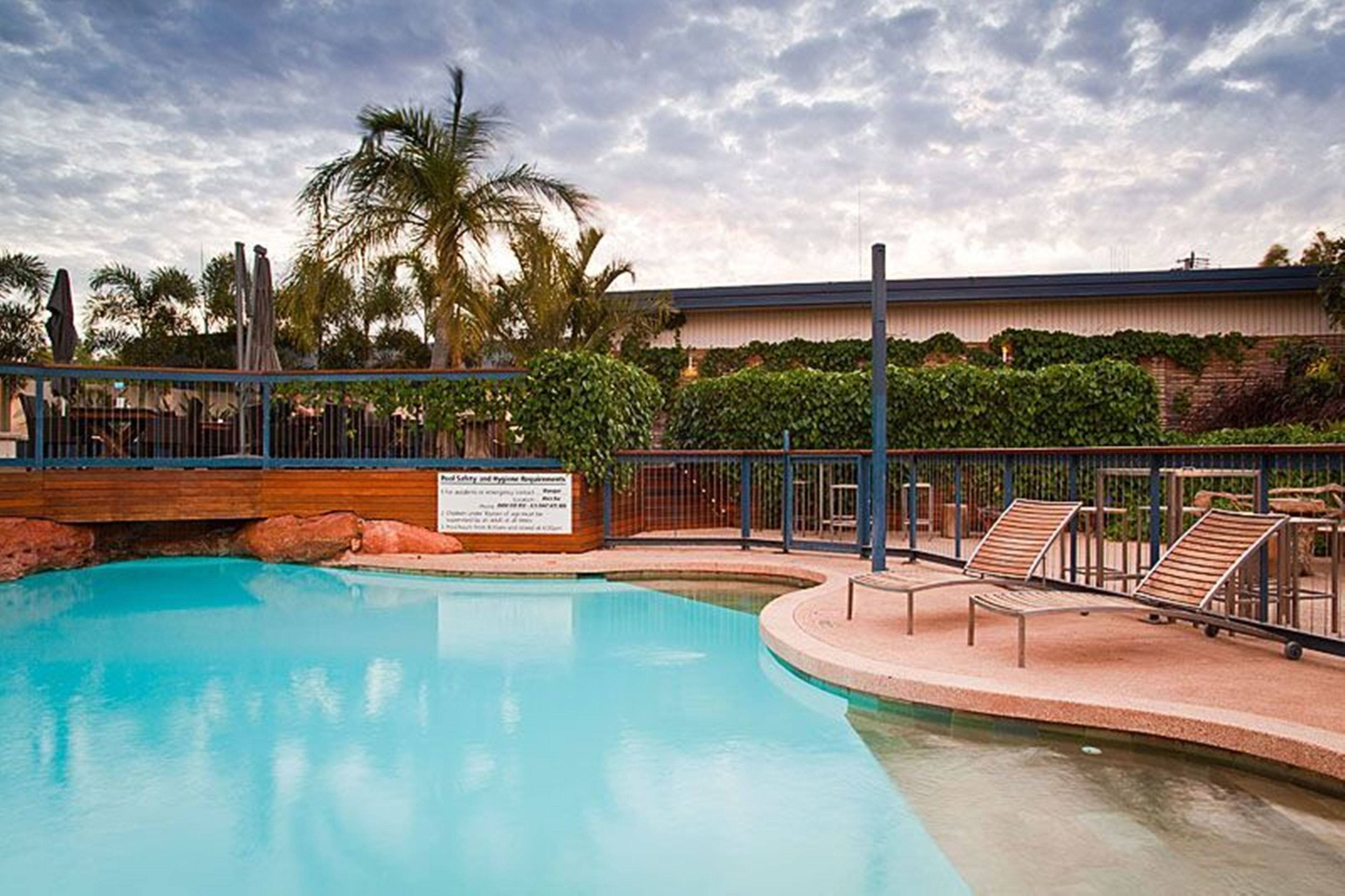 A swimming pool with lounge chairs, palm trees, and a fenced area with a sign.