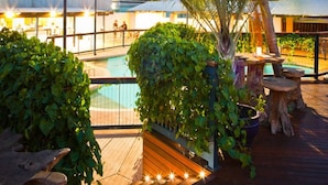 Una terraza de madera con piscina, rodeada de exuberante vegetación y palmeras.