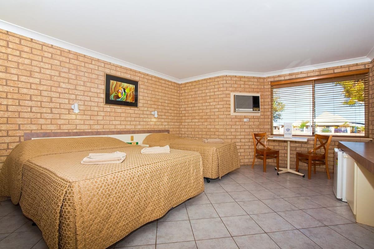 Une chambre d’hôtel avec deux lits, une télévision, une fenêtre avec des stores et une petite table avec des chaises.