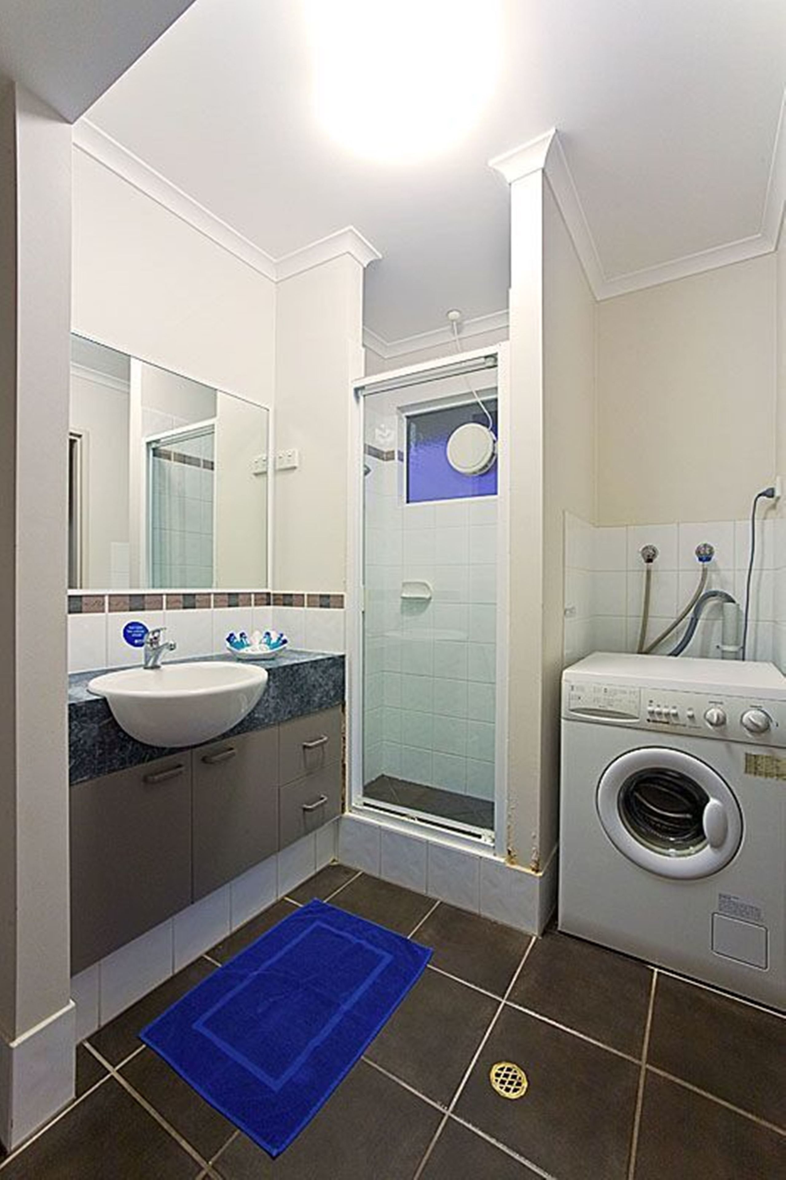 Een kleine badkamer met een wastafel, spiegel, douche en wasmachine.
