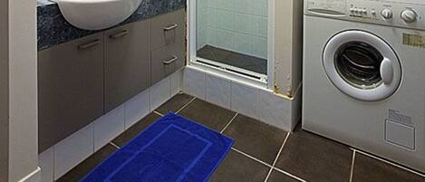 Een kleine badkamer met een wastafel, spiegel, douche en wasmachine.