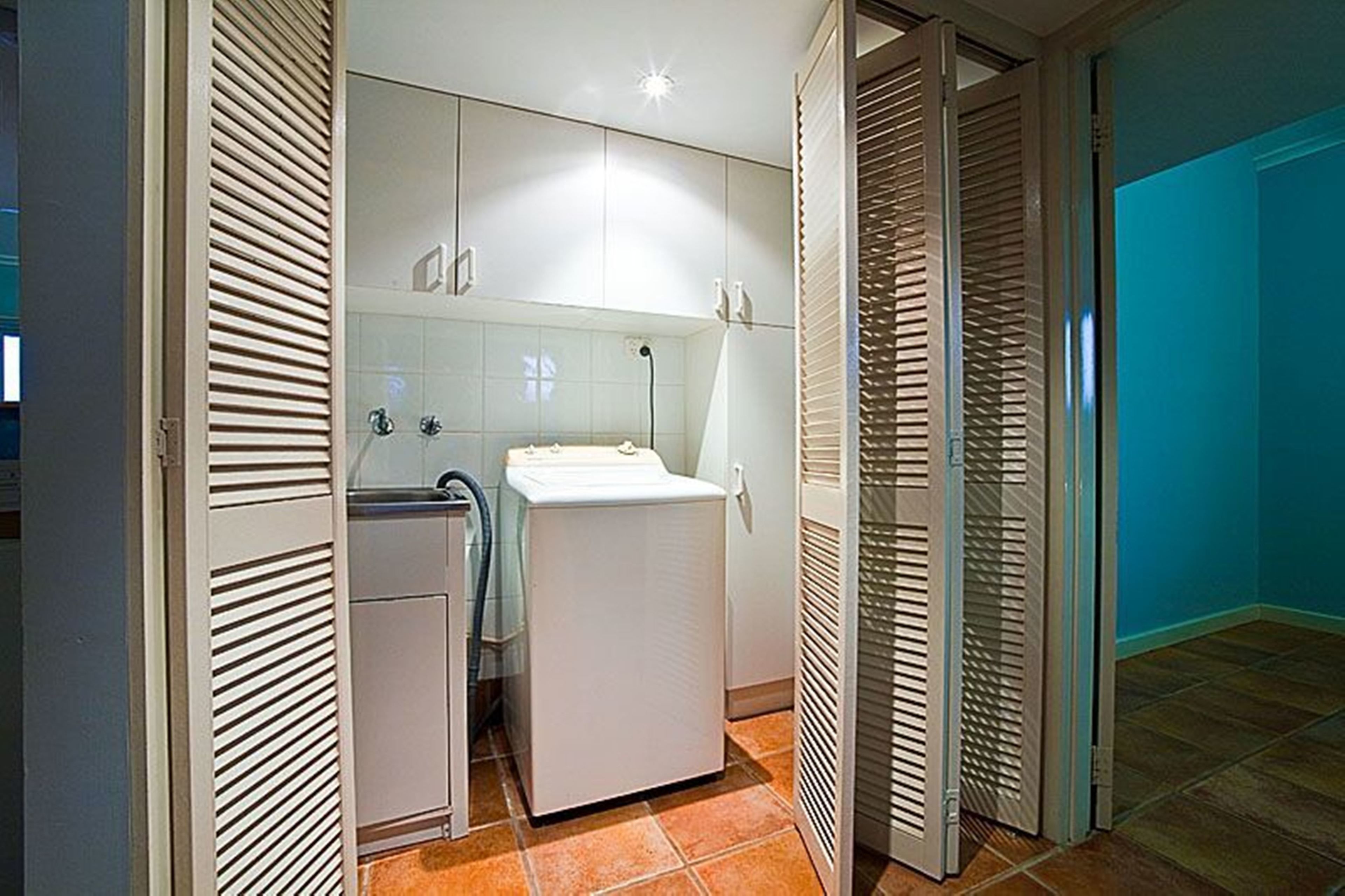 A compact bathroom with a built-in washing machine, a sink, and a shower area.