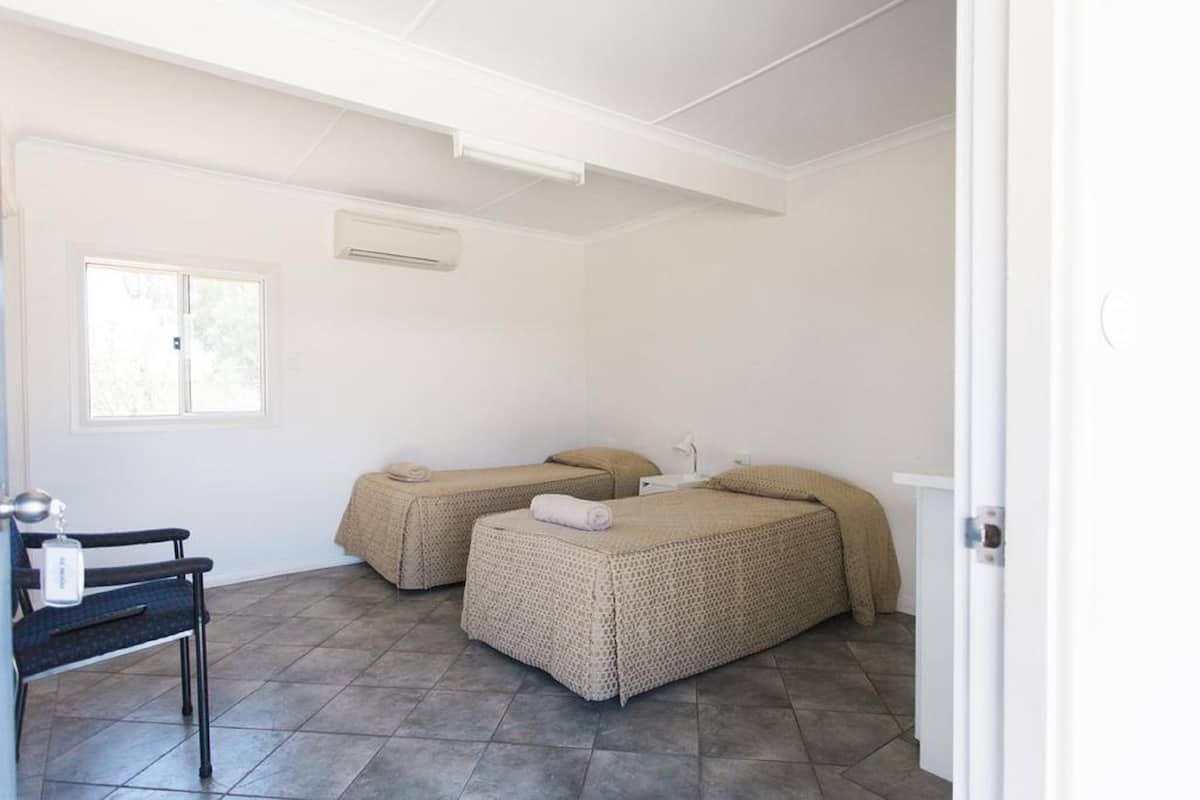 Une chambre avec deux lits, une chaise et une fenêtre.
