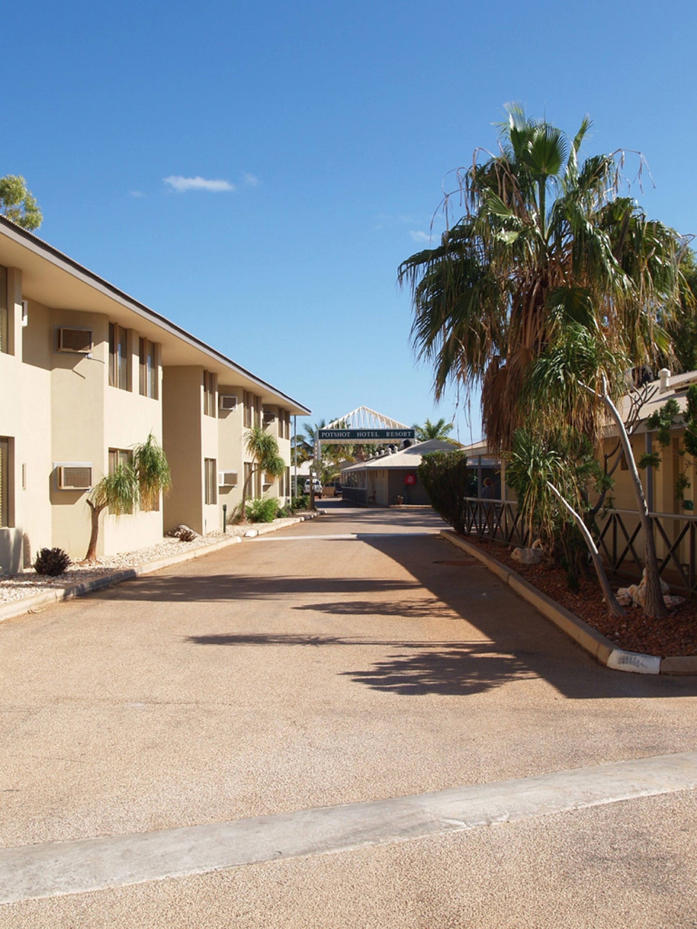 A hotel with a central courtyard, palm trees, and a clear sky.