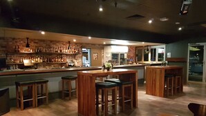 Una zona de bar con taburetes de madera, una barra con una caja registradora y estantes llenos de botellas.