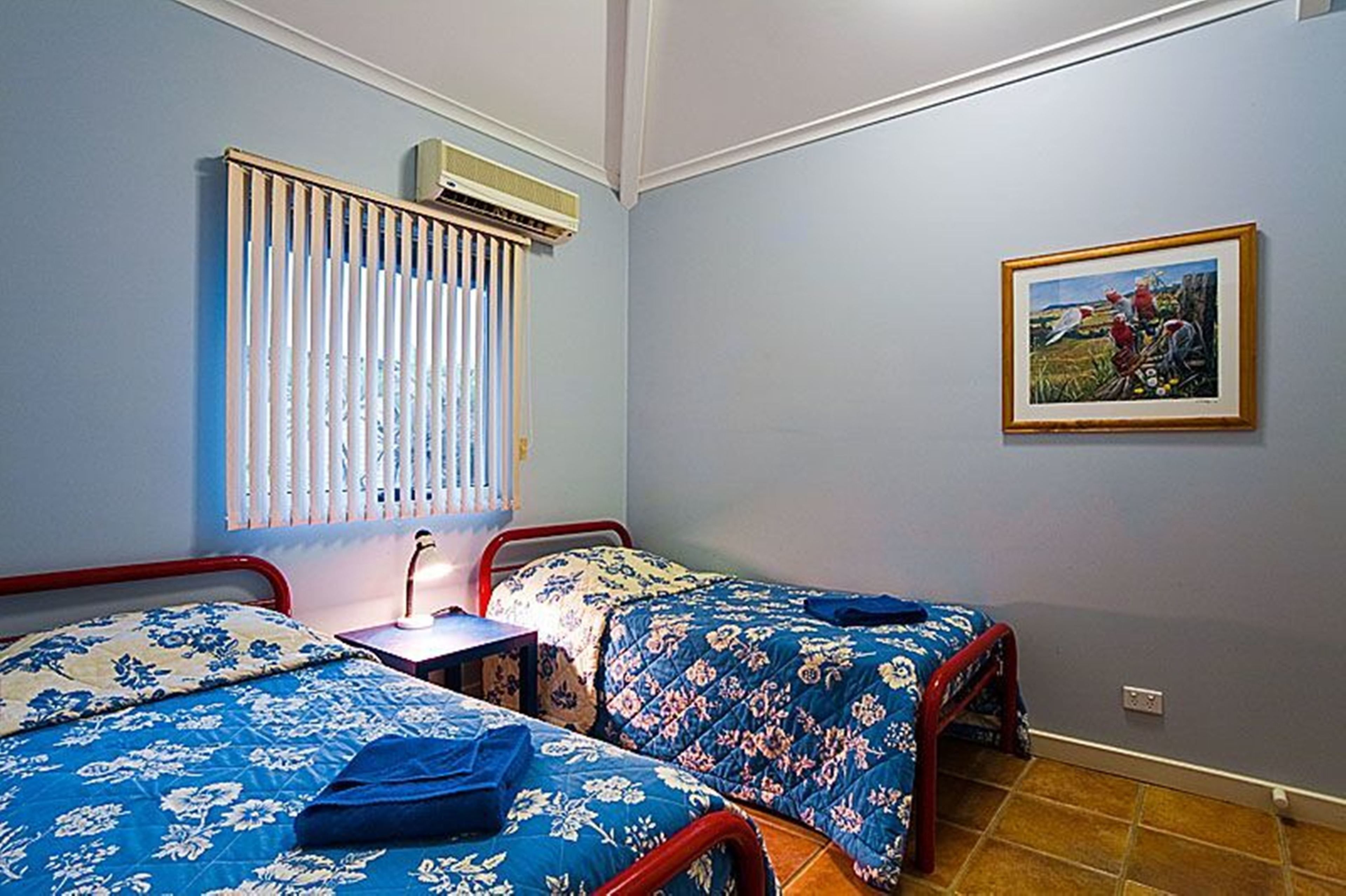 Une chambre avec deux lits, une table de chevet, un climatiseur et un tableau encadré au mur.