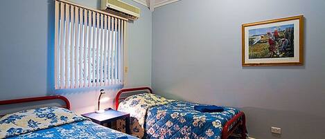 Une chambre avec deux lits, une table de chevet, un climatiseur et un tableau encadré au mur.