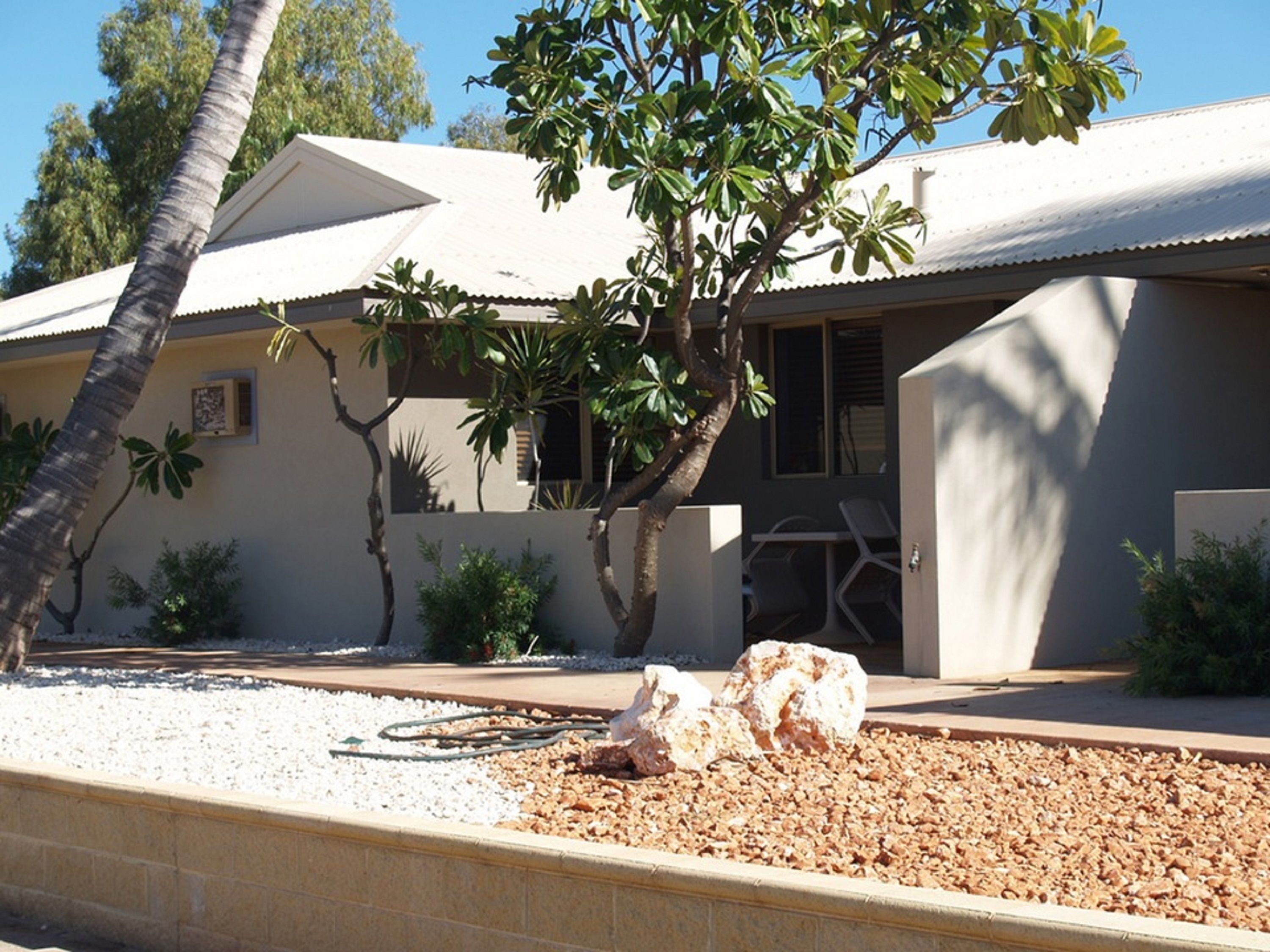 A modern house with a white exterior, a covered patio, and a small garden area with gravel and mulch.
