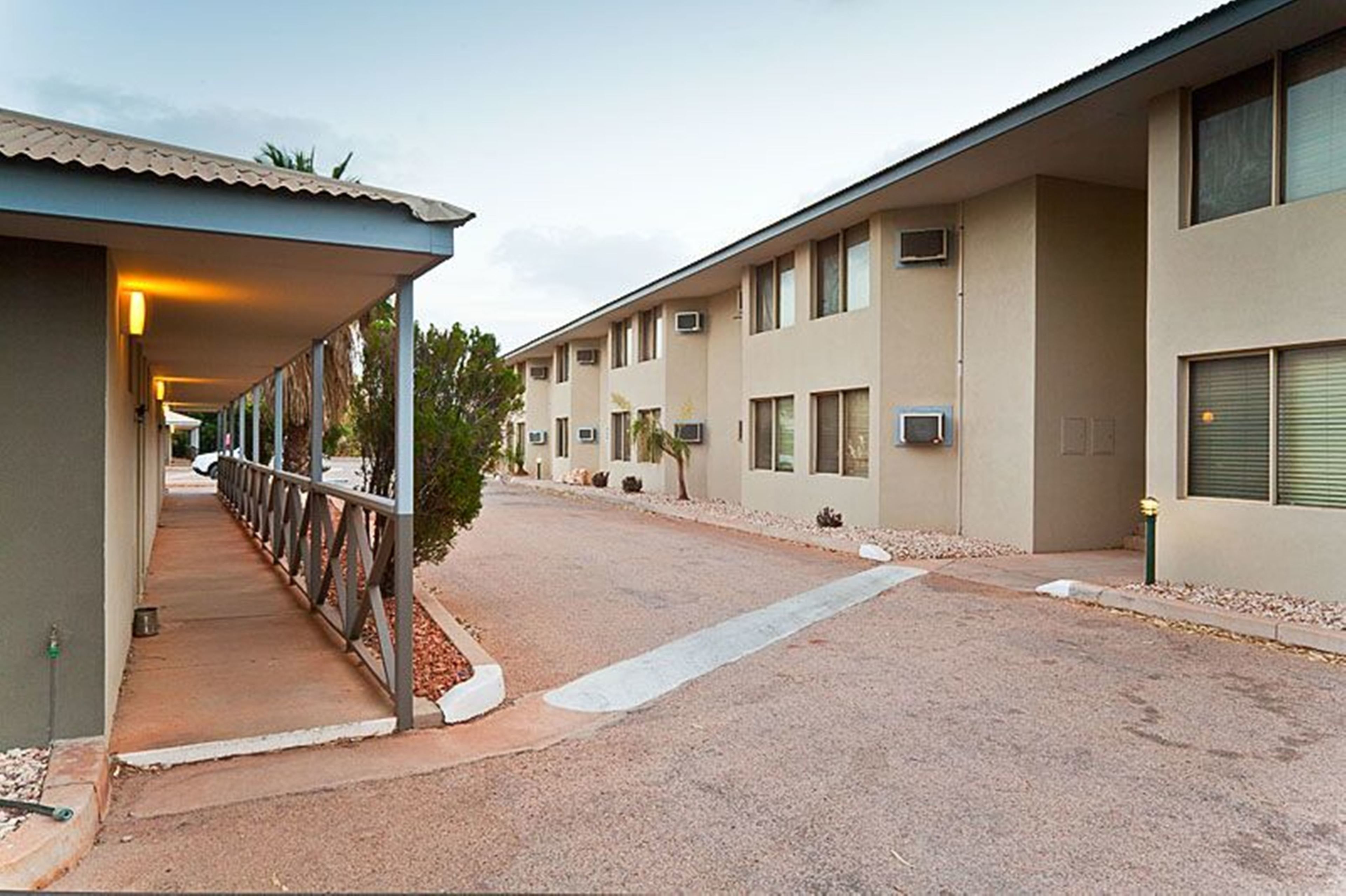 A row of motel rooms with a covered walkway and a gravel driveway.